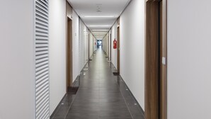 A long, narrow hallway with a tiled floor, flanked by walls with vertical blinds and wooden doors.