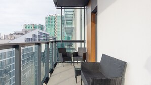 A balcony with wicker furniture, a glass railing, and a view of city buildings.