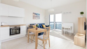 A modern kitchen with white cabinets, a built-in oven, and a dining area with a wooden table and chairs.