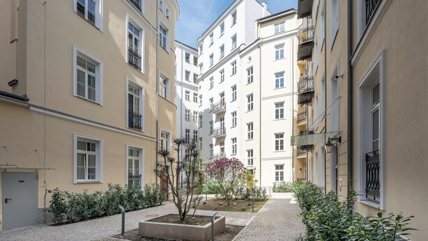 A courtyard with a central garden, surrounded by multi-story buildings with balconies and windows. - Piękna 2-Bedroom Apartment (Warszawa)