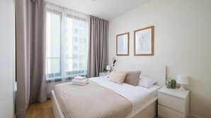 A neatly arranged bedroom with a large bed, a bedside table with a lamp, and two framed pictures on the wall.