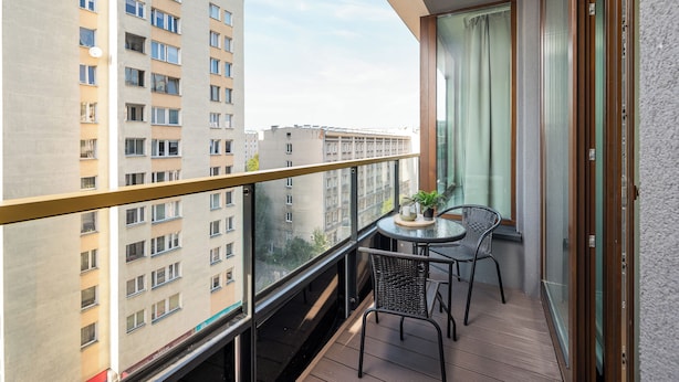 A balcony with a table and chairs, overlooking a cityscape with high-rise buildings.