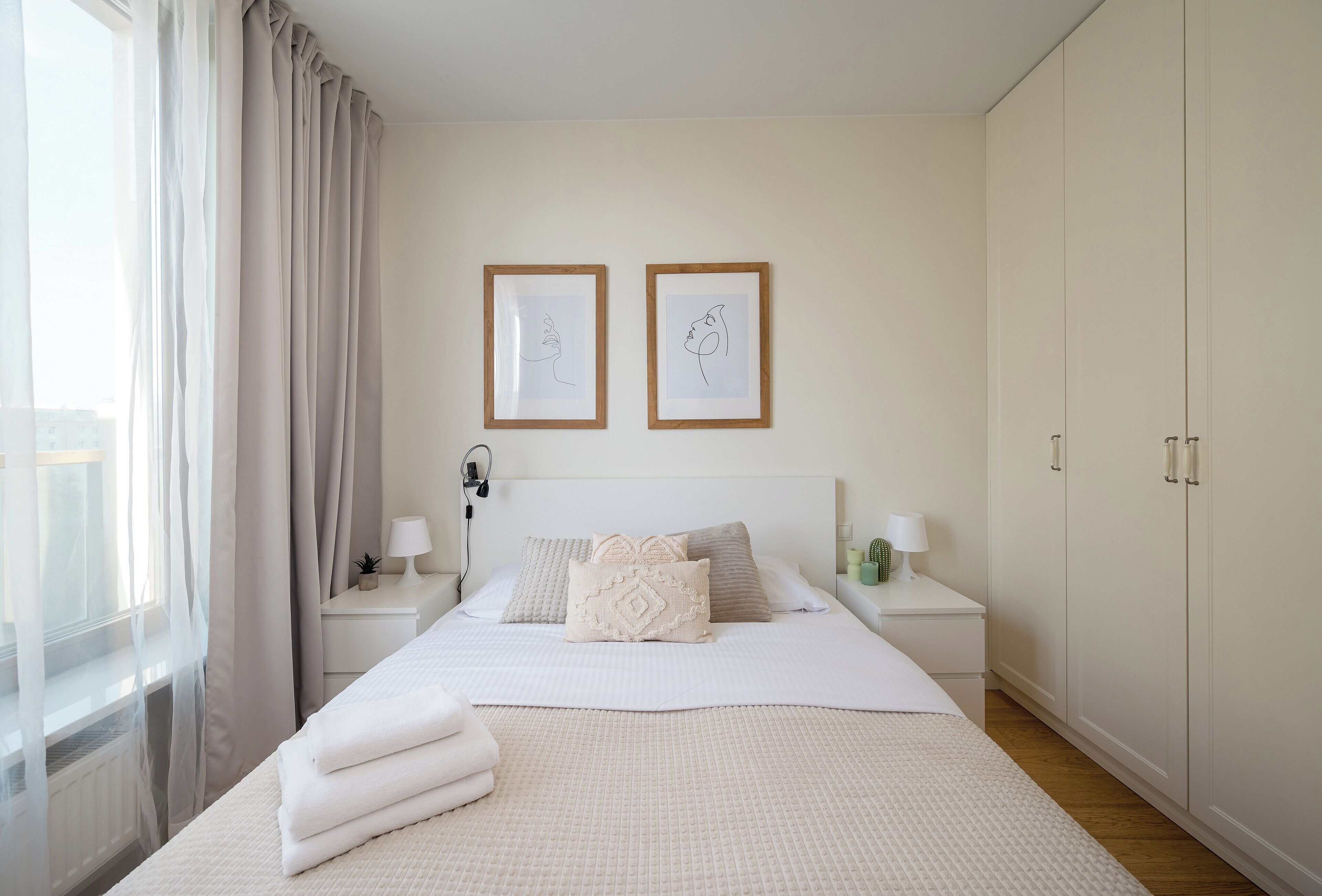 Une chambre à coucher bien rangée, avec un lit, des tables de chevet, une commode, une armoire et deux œuvres d’art encadrées accrochées au mur.