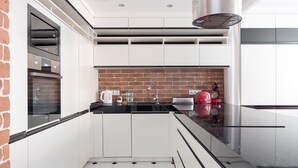 A modern kitchen with white cabinets, a brick backsplash, and a black countertop. - Old Town Grey Apartment (Warszawa)