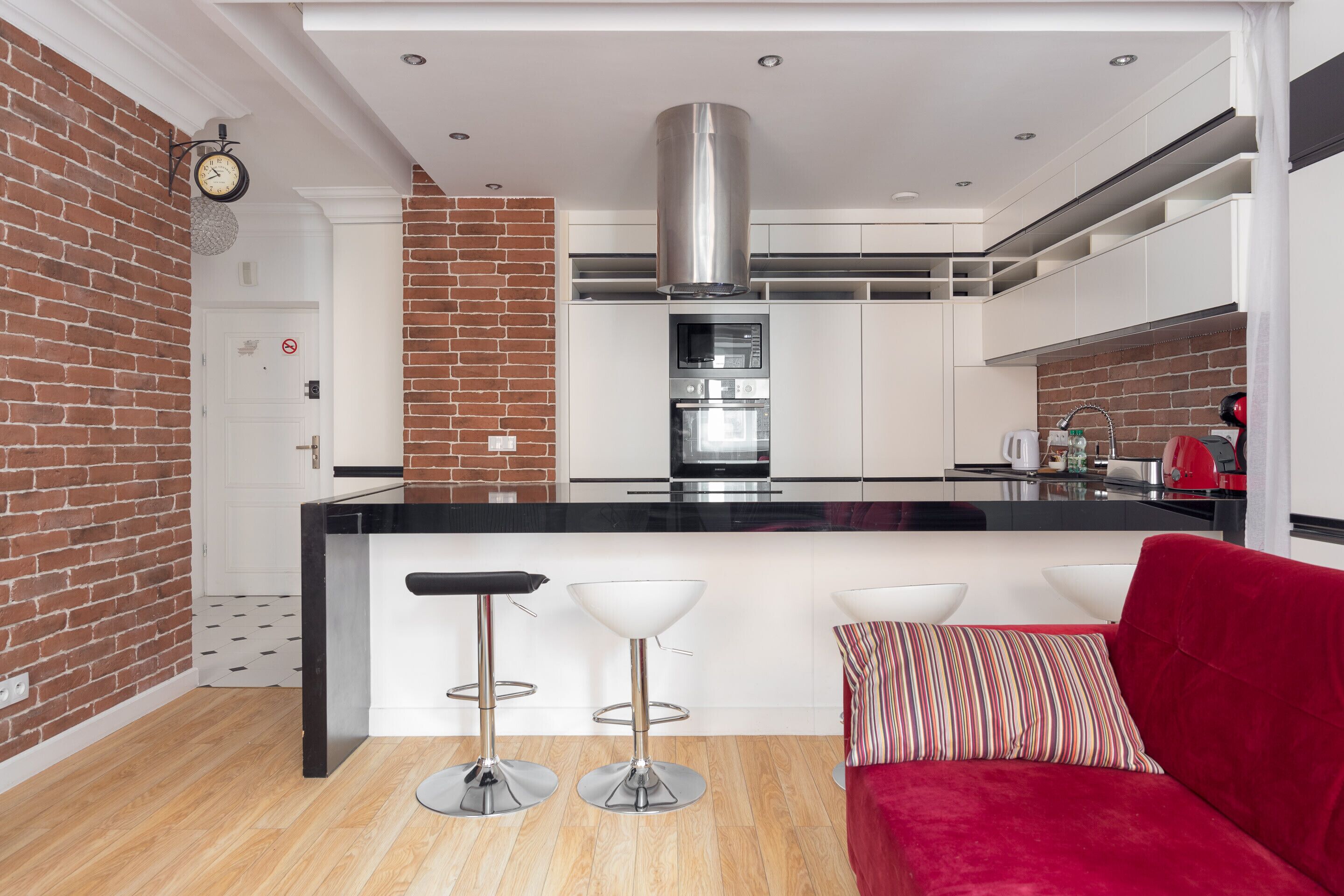 Una cucina moderna con isola centrale, due sgabelli da bar e un divano rosso.