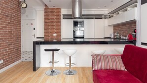 A modern kitchen with a central island, two bar stools, and a red sofa. - Old Town Grey Apartment (Warszawa)