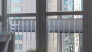 Habitación con vista a un edificio a través de una ventana. Hay una silla y una mesa con una planta encima.