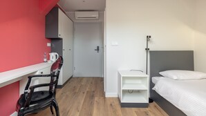 A compact hotel room with a bed, a desk, a chair, and a kitchenette.