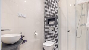 A modern bathroom with a large white sink, a toilet, and a glass-enclosed shower area.