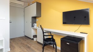 A compact room with a white desk, a black chair, a flat-screen TV mounted on the wall, a small black refrigerator, and a white cabinet with a coffee maker. - ĄĘ Hostel  Nowy Świat (Warszawa)