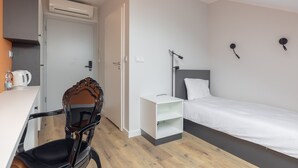 A modern hotel room with a bed, a desk, a chair, and a small white nightstand. - ĄĘ Hostel Nowy Świat (Warszawa)