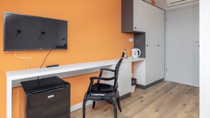 A compact room with a white desk, a black chair, a television mounted on the wall, and a small refrigerator. - ĄĘ Hostel Nowy Świat (Warszawa)