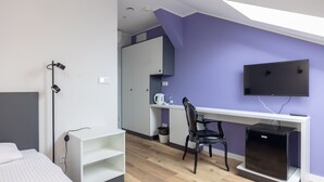 A modern room with a bed, a desk, a chair, a TV, and a small refrigerator.