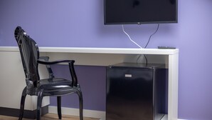 A room with a white desk, a black chair, a flat-screen TV mounted on the wall, and a small black appliance on the desk.