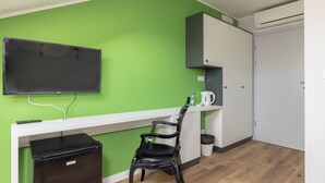 A room with a green wall, a white desk, a black chair, a television, a white cabinet, and a white door. - ĄĘ Hostel Nowy Świat (Warszawa)