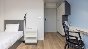 Een slaapkamer met een bed, nachtkastje, lamp en een bureau met stoel.
