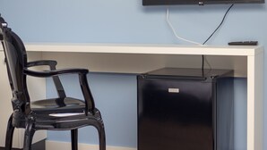 Een kamer met een bureau, een stoel, een aan de muur bevestigde televisie en een kleine, zwarte koelkast.