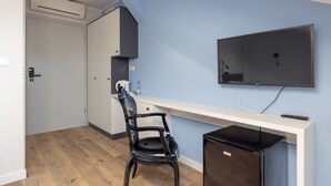 Een compacte kamer met een kitchenette, een flatscreen televisie aan de muur, een zwarte stoel en een kleine koelkast.