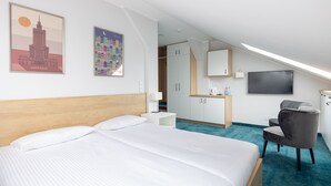 A hotel room with a large bed, a desk with a chair, a TV, and artwork on the walls.