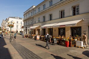 A street with cafes and shops, a pedestrian, and a bicycle. - Aparthotel Esencja Warszawy 15 NowyŚwiat (Warszawa)