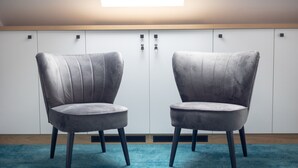Two grey upholstered chairs with black legs, positioned on a blue carpet in front of a white wardrobe with a wooden top and two black handles.