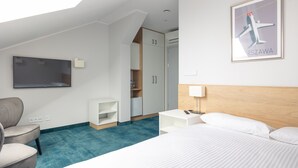 A hotel room with a bed, a desk, a chair, a TV, and a wardrobe.
