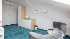 A modern, minimalist room with a blue carpet, a wooden cabinet, a grey armchair, and a small table.