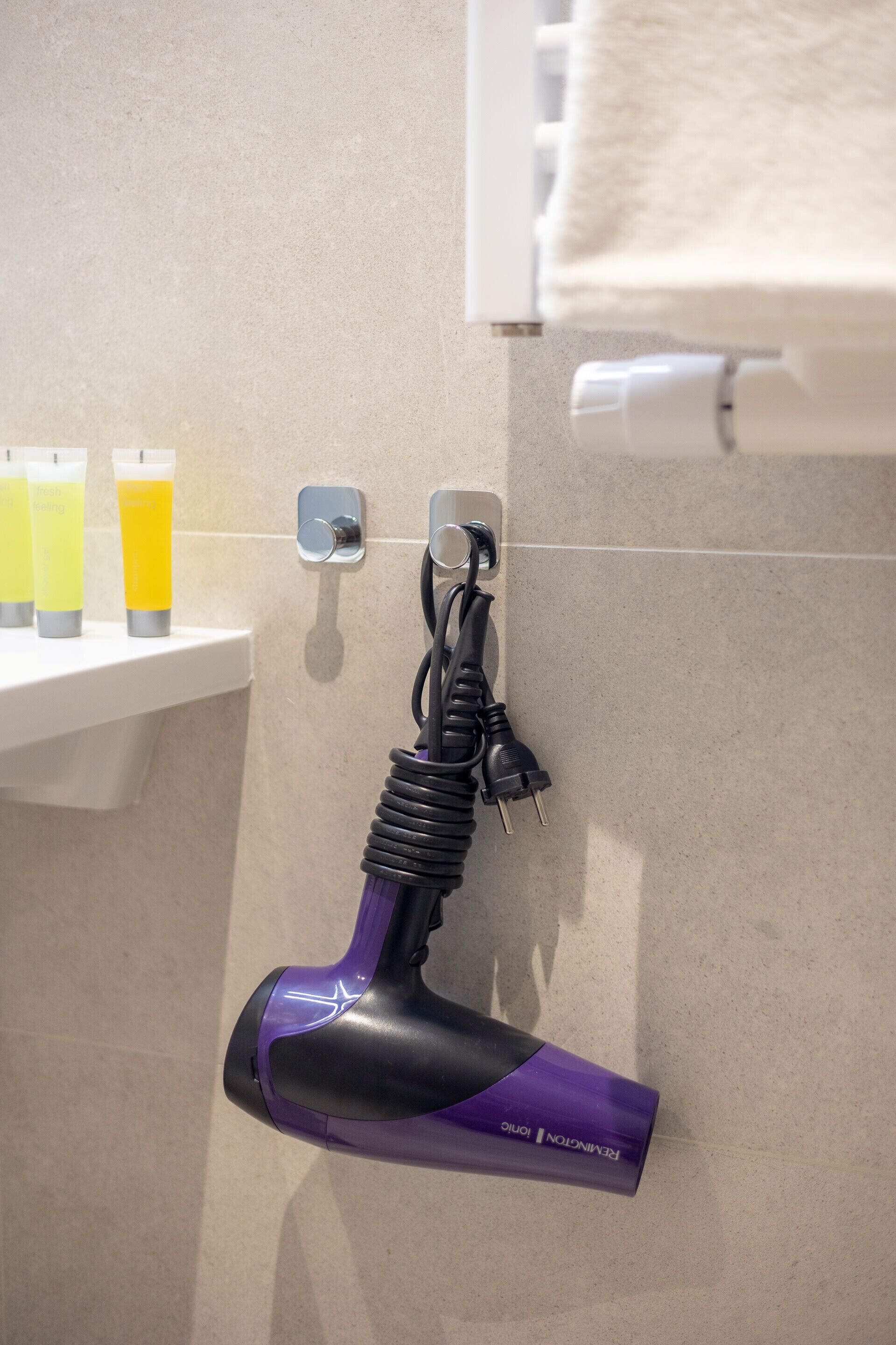 Un sèche-cheveux fixé au mur, une serviette suspendue à un porte-serviettes et une étagère avec des bouteilles.