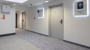 A hotel corridor with doors, emergency equipment, and illuminated signs indicating room numbers and amenities.