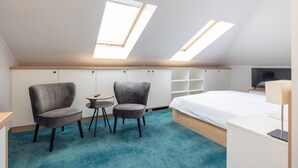 A modern hotel room with a large bed, two armchairs, a small table, and a TV. There are skylights on the ceiling.