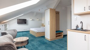 Une chambre d’hôtel moderne dotée d’un lit en mezzanine, d’un bureau, d’une kitchenette et d’une grande fenêtre laissant entrer la lumière naturelle.