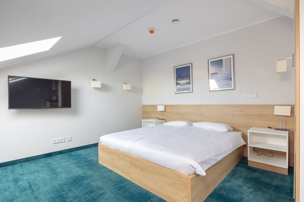 Una habitación de hotel moderna con una cama grande, un televisor de pantalla plana montado en la pared y dos cuadros enmarcados.