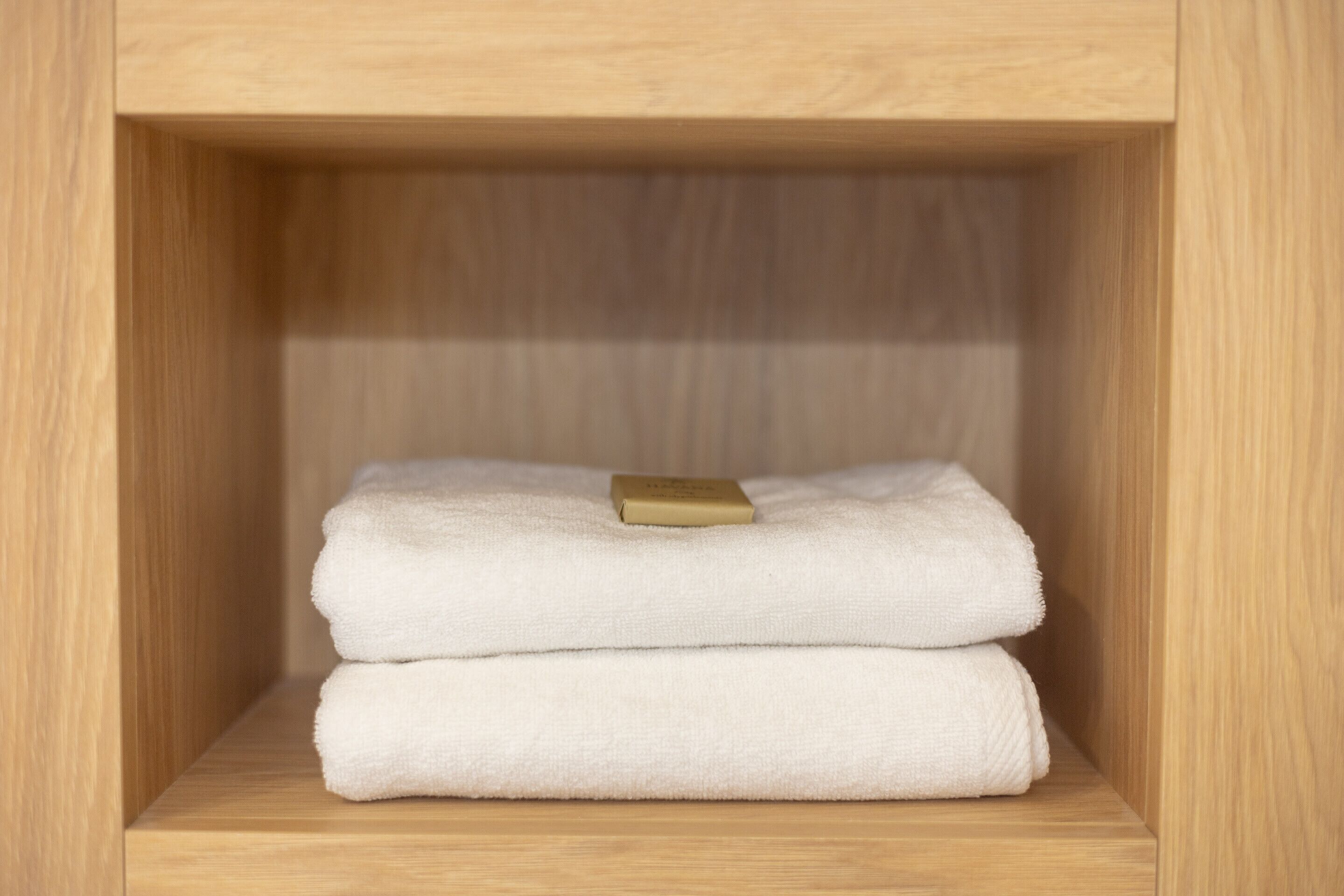 A wooden shelf with two folded white towels and a small rectangular object on top.