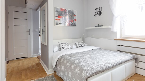 Ein Schlafzimmer mit einem Bett, einer weißen Tür, einem Wandbild und einem Regal mit einem Traumfänger.