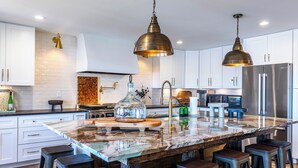 A modern kitchen with white cabinets, a large island with bar stools, stainless steel appliances, and pendant lighting. - Lake Oconee lake front with pool (Eatonton)