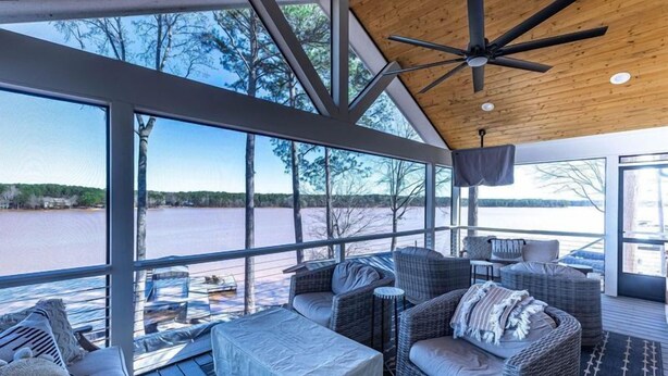 A covered outdoor seating area with wicker furniture, large windows, and a view of a lake. - Lake Oconee lake front with pool (Eatonton)