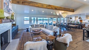 A spacious living area with a fireplace, large windows, and a kitchen in the background. - Lake Oconee lake front with pool (Eatonton)