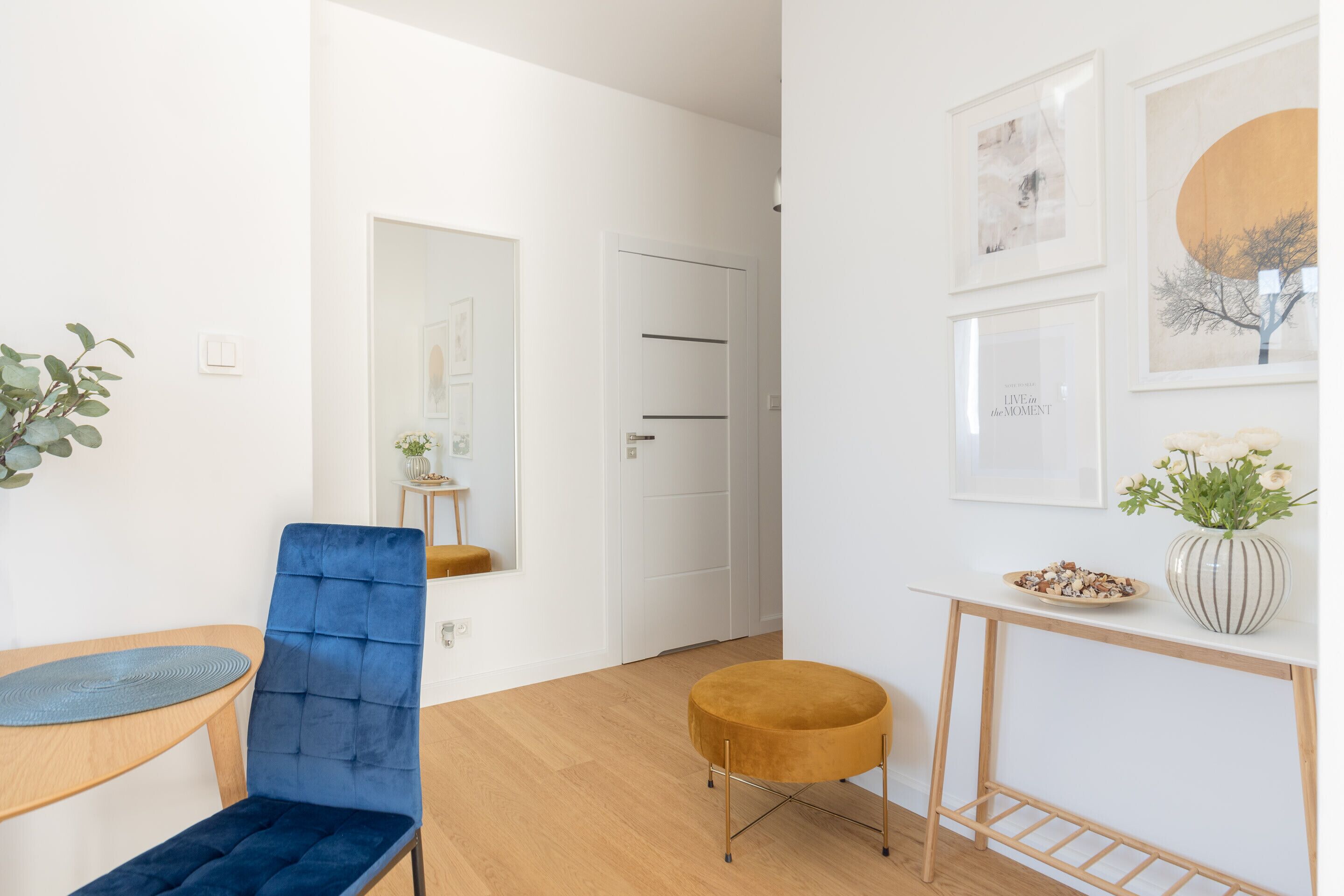A modern room with a blue chair, a round ottoman, a wooden table, and a console table with a vase and bowl.