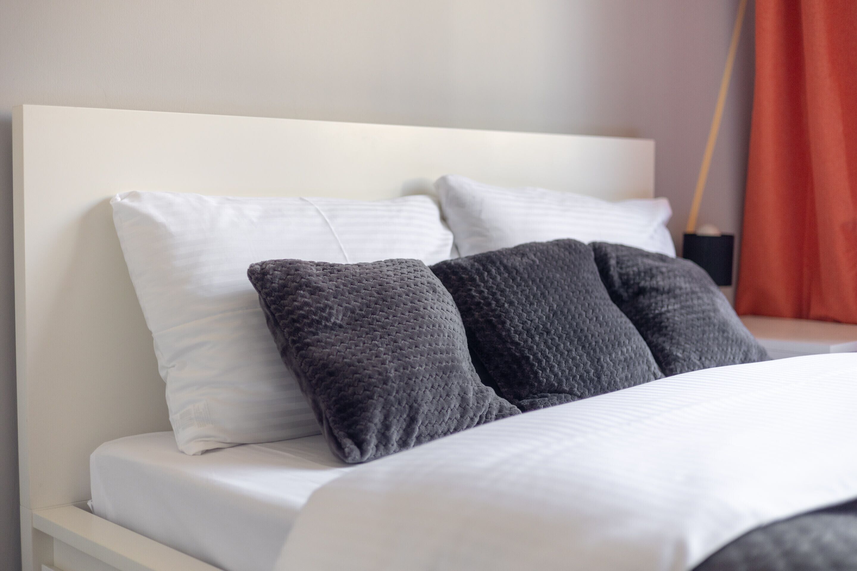 A bed with white and gray pillows, a white headboard, and a red curtain in the background.