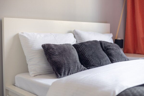 A bed with white and gray pillows, a white headboard, and a red curtain in the background.