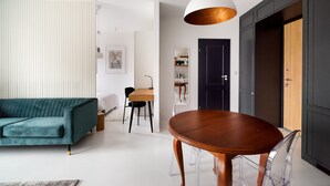 Un salon moderne avec un canapé de couleur turquoise, une table à manger en bois et des chaises transparentes, ainsi qu’un grand luminaire suspendu blanc.