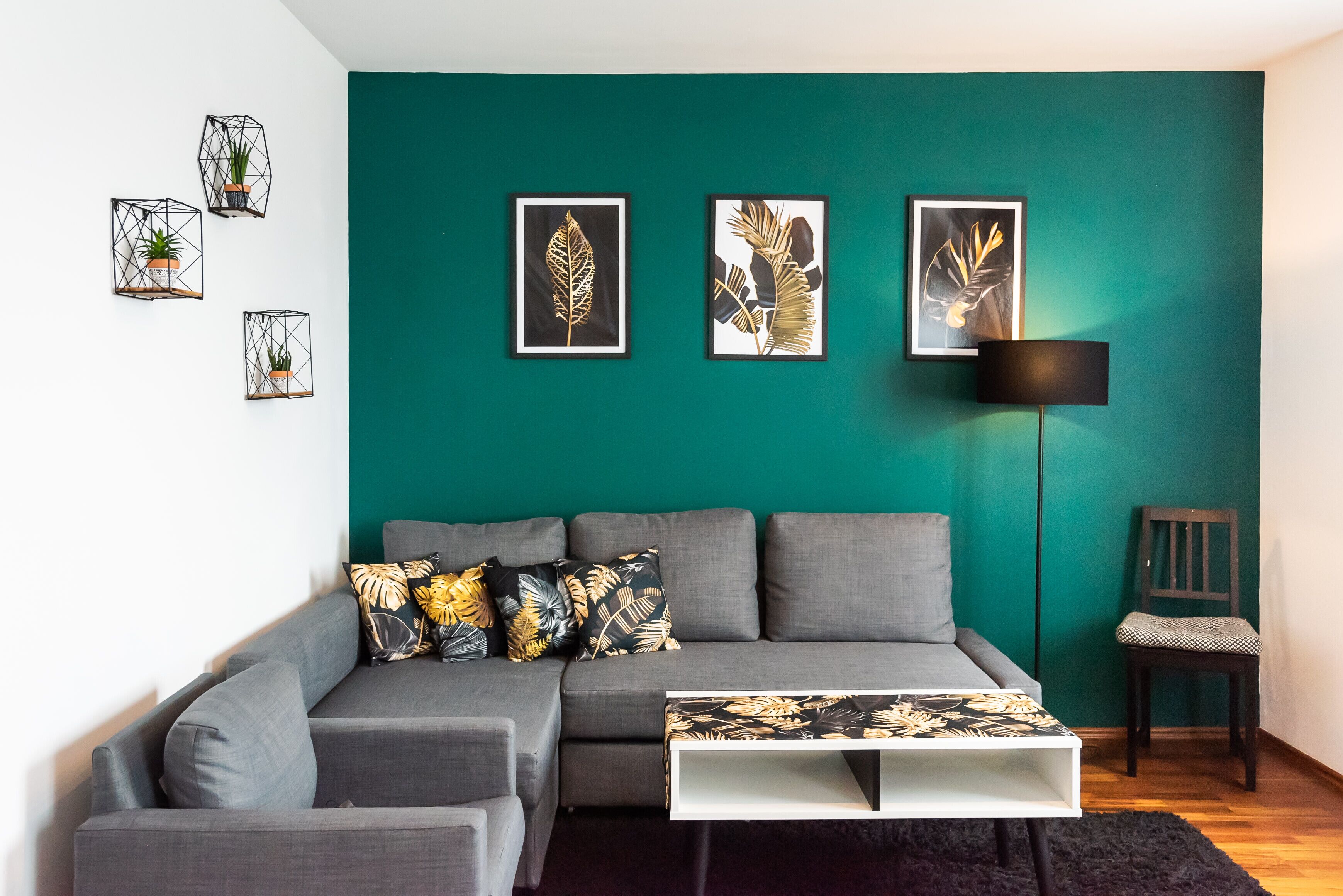 Una sala de estar moderna con una pared de acento color verde azulado, un sofá seccional gris y una mesa de centro blanca.