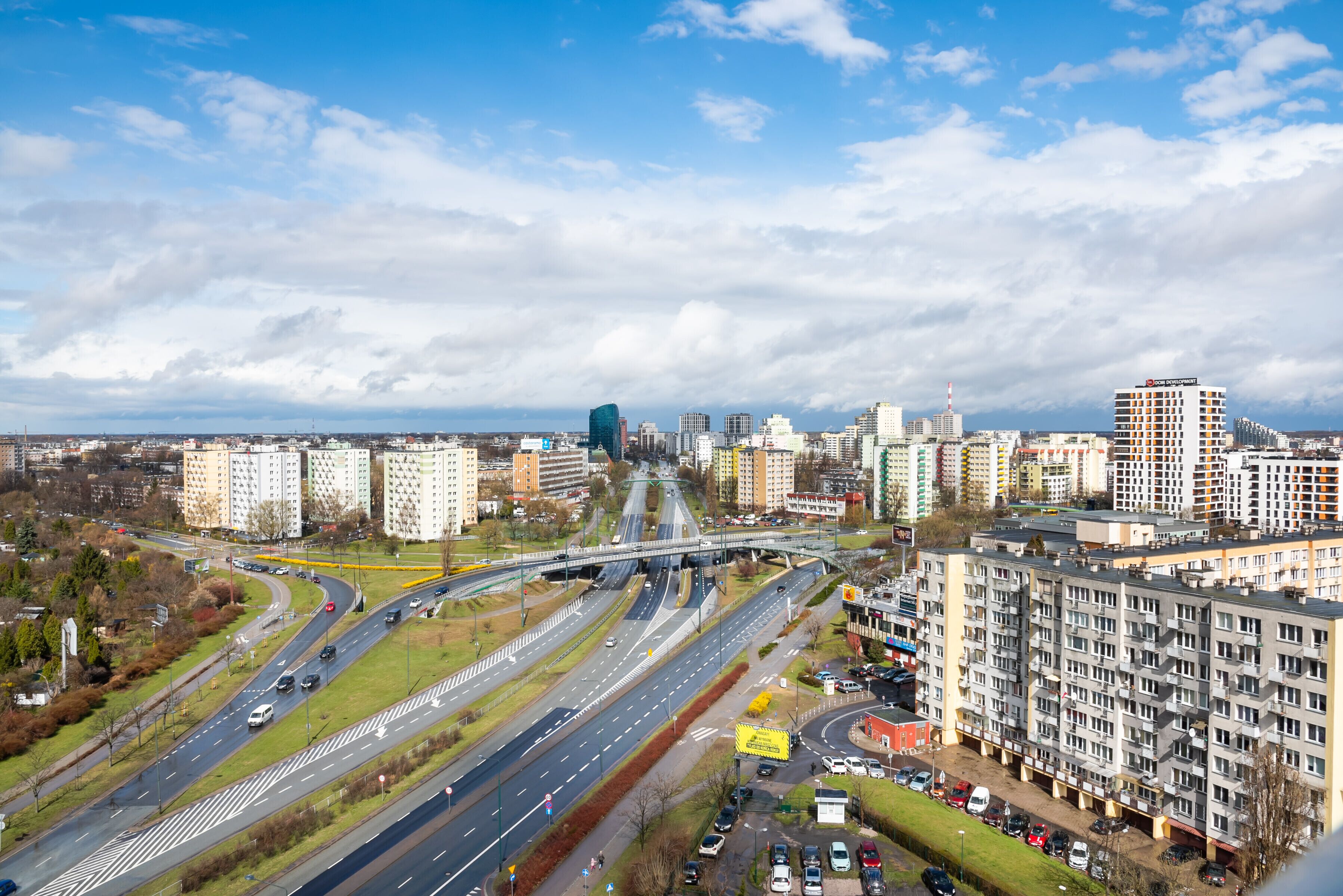 Un paysage urbain avec de nombreux immeubles de grande hauteur, une autoroute à plusieurs voies et un pont piétonnier.