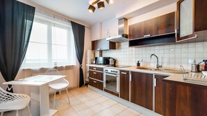 A modern kitchen with wooden cabinets, a built-in oven, and a dining area with a white table and chairs. - Saska Kępa Malachite Studio (Warszawa)