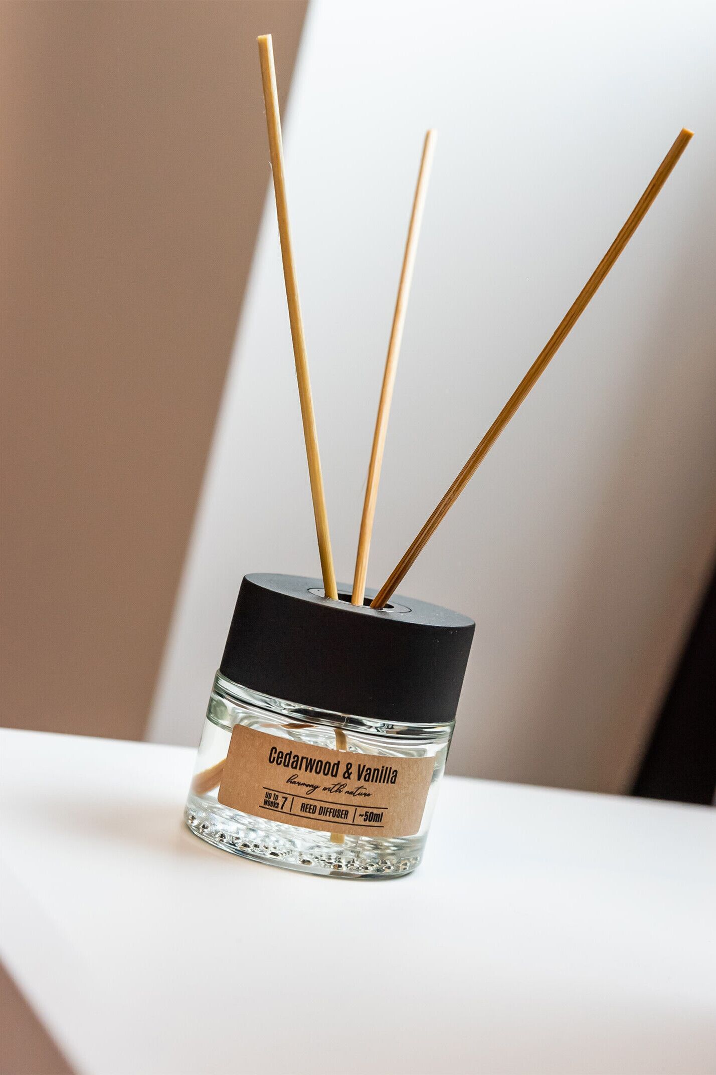Un difusor de vidrio con palitos de madera, etiquetado 'Cedarwood & Vanilla', sobre una superficie blanca.