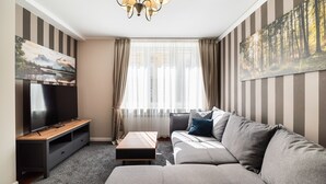 Ein modernes Wohnzimmer mit einem großen Flachbildfernseher, einem grauen Sofa, einem Holztisch und rauen Wänden mit Streifenmuster.