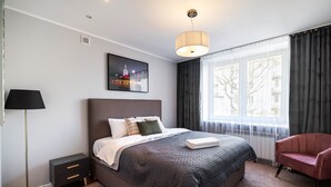 Ein modernes Schlafzimmer mit einem großen Bett, einem Nachttisch, einer Stehlampe, einem Sessel und einem Fenster mit Vorhängen.