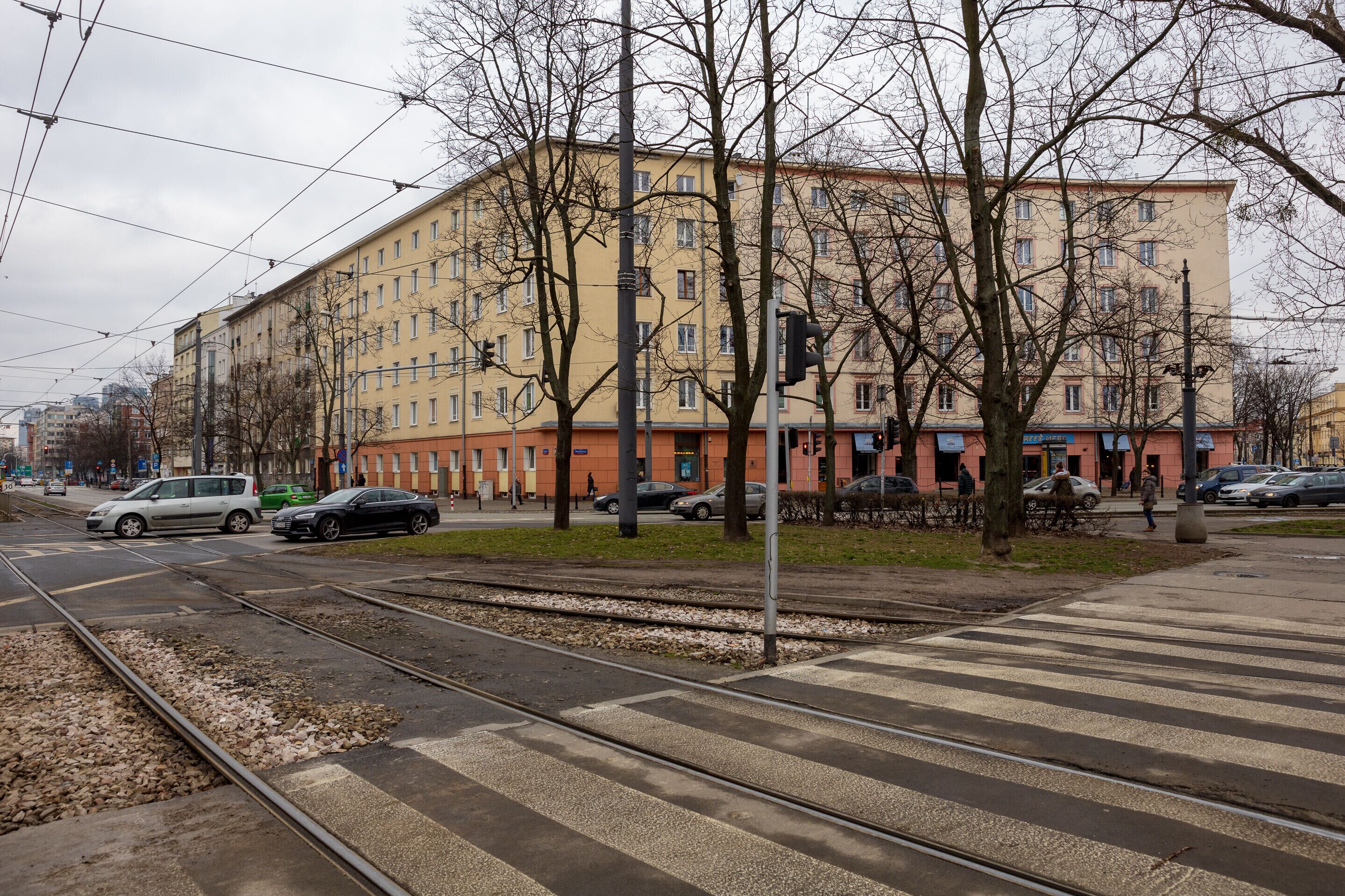 A multi-story building with a yellow facade, located near a tram line.