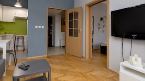 Ein modernes Wohnzimmer mit Flachbildfernseher, einem Esstisch und einer Küchenzeile im Hintergrund.