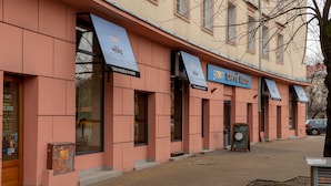 Ein Gebäude mit rosafarbener Fassade und Markisen, auf denen die Beschilderung 'Caffè Nero' zu sehen ist.